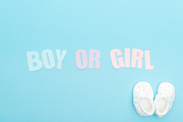 bovenaanzicht van booties en jongen of meisje belettering op blauwe achtergrond met kopieerruimte - Foto, afbeelding