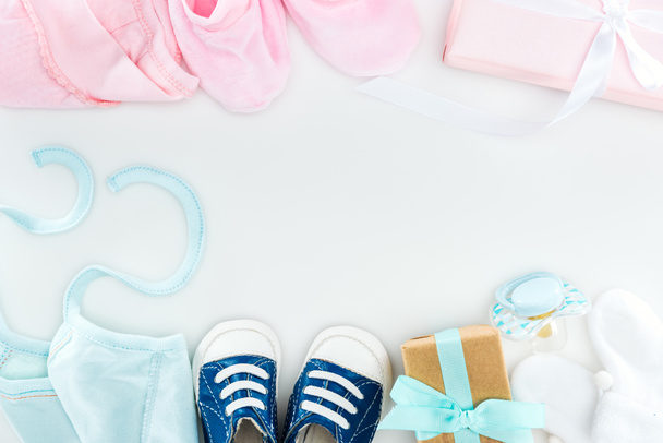 top view of booties and sneakers, pacifier, gift boxes and bonnets on white background - Photo, Image