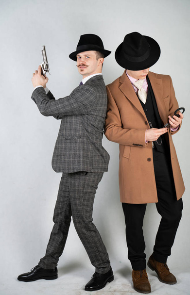 twee vrienden gekleed in vintage kleding en verbeelden retro detectives en spionnen in Engelse klassieke stijl op een witte studio achtergrond - Foto, afbeelding
