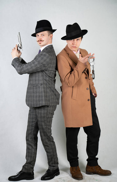 δύο φίλοι ντυμένοι με ρούχα vintage και απεικονίζουν ρετρό ντετέκτιβ και κατασκόπους σε αγγλικό κλασικό στιλ σε ένα φόντο λευκό στούντιο - Φωτογραφία, εικόνα