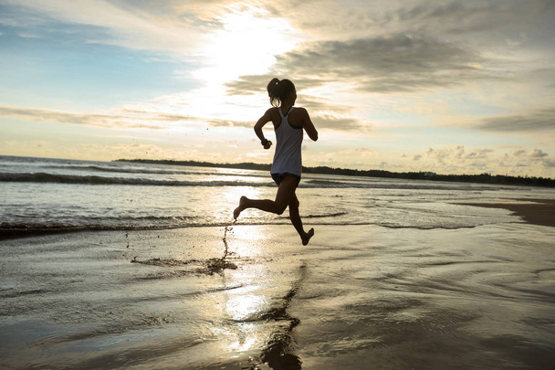 Female athlete running at sunset on beach - Foto, Imagem