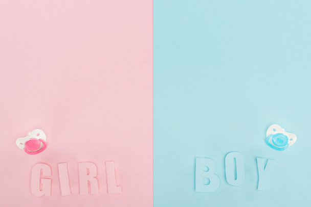 bovenaanzicht van fopspenen, jongen, meisje belettering op roze en blauwe achtergrond met kopieerruimte - Foto, afbeelding