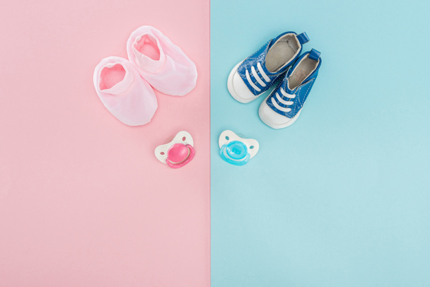 top view of pacifiers, booties, sneakers on pink and blue background with copy space - Photo, Image