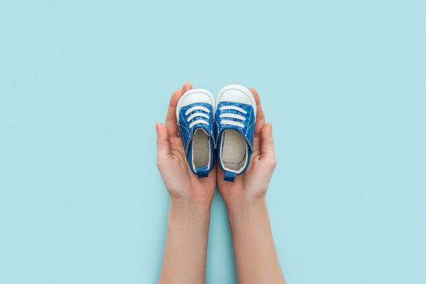 partial view of adult man holding sneakers on blue background with copy space - Fotó, kép