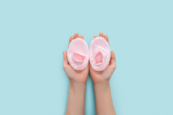 partial view of adult woman holding pink booties on blue background with copy space - Photo, Image