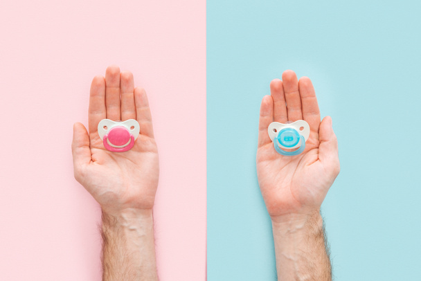 cropped view of men holding pacifiers on blue and pink background with copy space - Foto, imagen