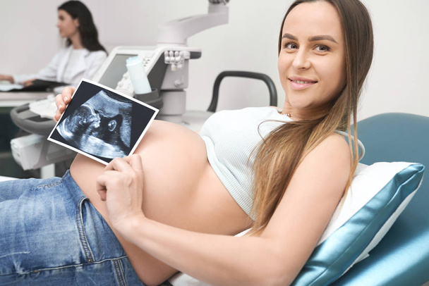 Szczęśliwa Kobieta w ciąży, pozowanie, Wyświetlono USG. - Zdjęcie, obraz