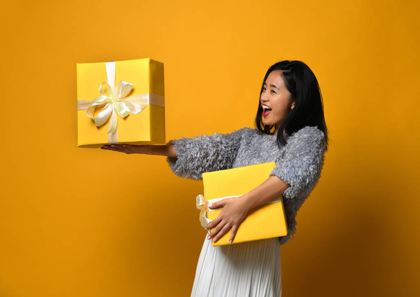Portrait of a smiling pretty girl holding two gift boxes isolated over yellow background - Zdjęcie, obraz