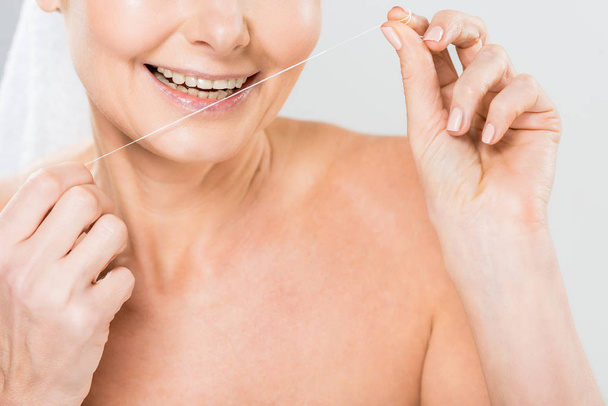 Selektivní fokus zralá žena čištění zubů s dentální nit izolované Grey - Fotografie, Obrázek