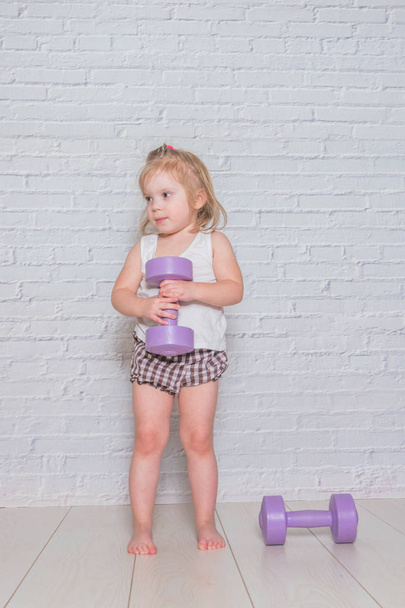 girl, the child is engaged in fitness with dumbbells, against a  - Photo, image