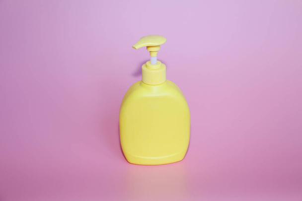 Yellow plastic bottle on a pink background. Yellow bottle with dispenser. - Foto, Bild