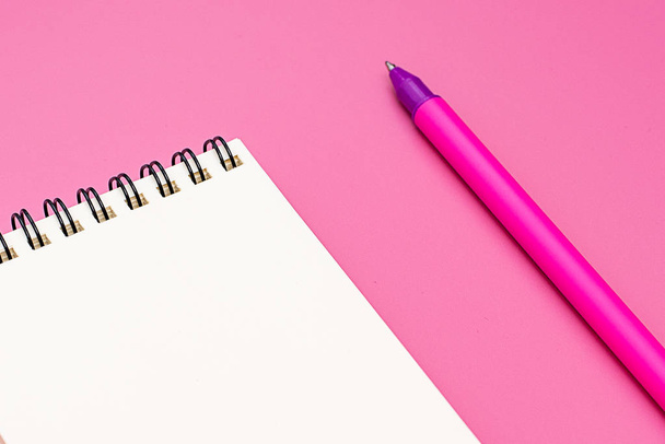 Cuaderno en blanco con espiral para la aplicación de etiquetas y bolígrafo sobre fondo rosa
 - Foto, imagen