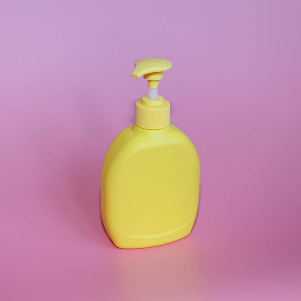 Yellow plastic bottle on a pink background. Yellow bottle with dispenser. - Fotó, kép