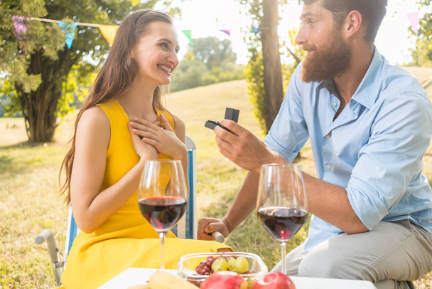 Man showing to beautiful girlfriend an engagement ring during romantic picnic - Foto, Imagen