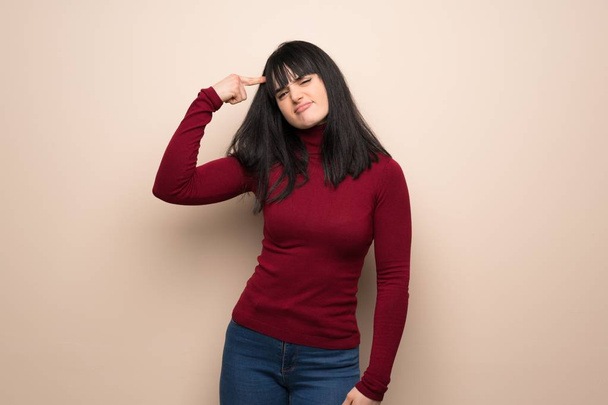Mujer joven con cuello alto rojo haciendo el gesto de locura poniendo el dedo en la cabeza
 - Foto, imagen
