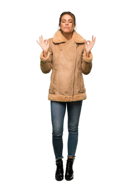 A full-length shot of a Blonde woman with a coat in zen pose over isolated white background - Photo, Image