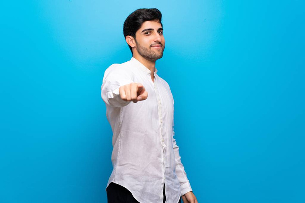 Jonge man over geïsoleerde blauwe muur vinger wijst op je met een vertrouwen uitdrukking - Foto, afbeelding