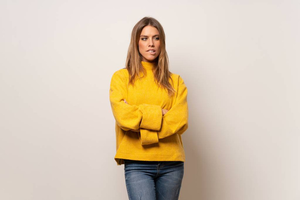 Woman with yellow sweater over isolated wall with confuse face expression while bites lip - Zdjęcie, obraz