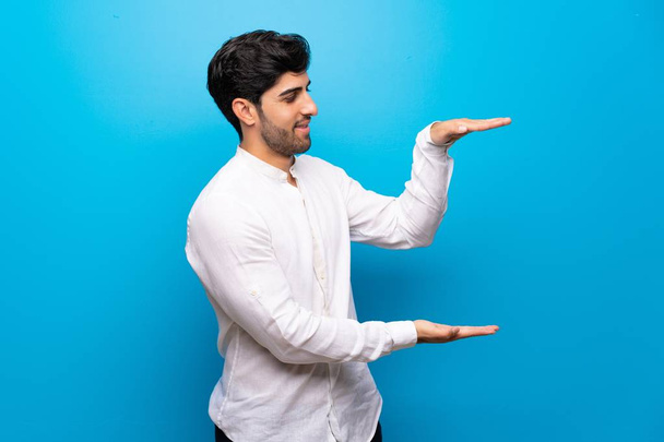 Bir reklam eklemek için izole mavi duvar tutan boşaltmak üzerinde genç adam - Fotoğraf, Görsel