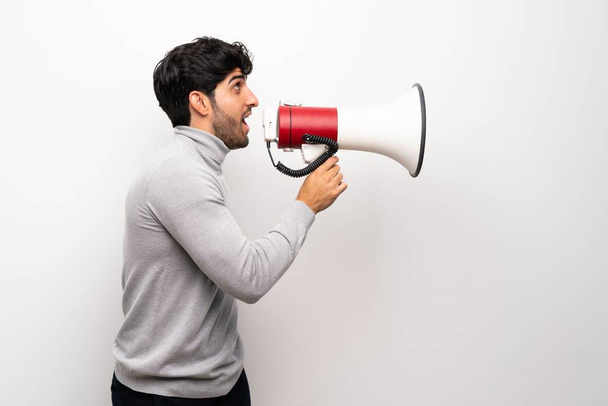 Молодой человек над изолированной белой стеной кричит через мегафон
 - Фото, изображение