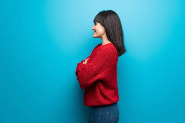 Woman with red sweater over blue wall in lateral position - Fotó, kép