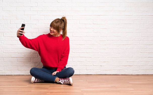 Κοκκινομάλλα γυναίκα χωροθέτηση στο πάτωμα φτιάχνοντας μια selfie - Φωτογραφία, εικόνα