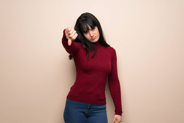 Fiatal nő, piros garbó mutatja hüvelykujját le jel negatív kifejezés - Fotó, kép