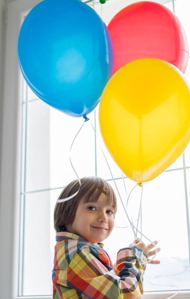 Boy with balloons in front of window  - Фото, изображение