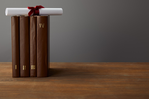 Brown books and diploma with red ribbon on wooden surface on grey - Photo, Image
