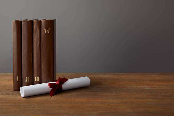 Livros castanhos e diploma com fita vermelha na superfície de madeira em cinza
 - Foto, Imagem