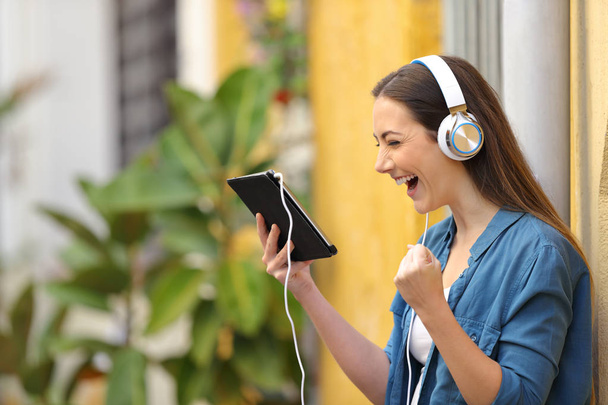 Excited woman wearing headphones watching tablet content - Zdjęcie, obraz
