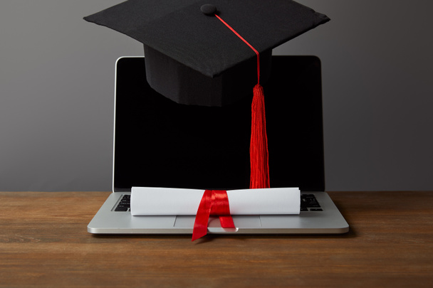 Přenosný počítač s prázdnou obrazovkou, diplomem a akademickým čepicí s červeným Tasselem na šedé - Fotografie, Obrázek