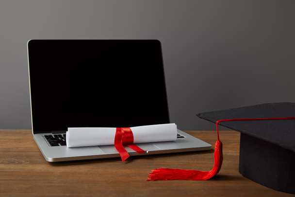 Laptop z pustym ekranem, dyplomem i kapelusza akademickiego z czerwonym pomponem na szarym - Zdjęcie, obraz