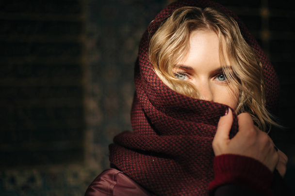 Photo of young blonde woman with scarf covered face against brown wall . - Φωτογραφία, εικόνα