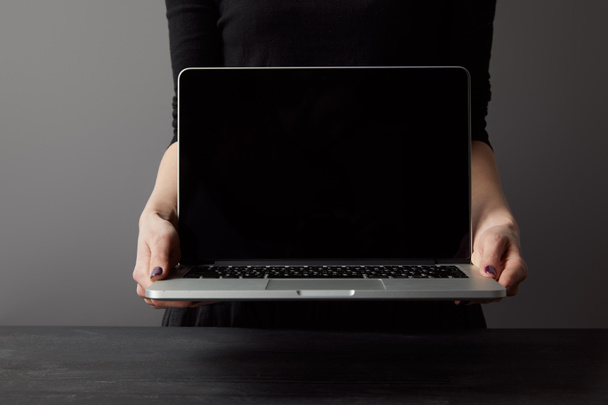 Partial view of woman holding laptop with blank screen on grey - Photo, Image