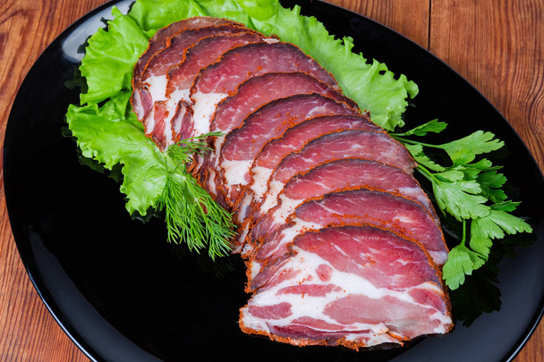 Collo di maiale secco affettato con verdure su piatto nero primo piano
 - Foto, immagini