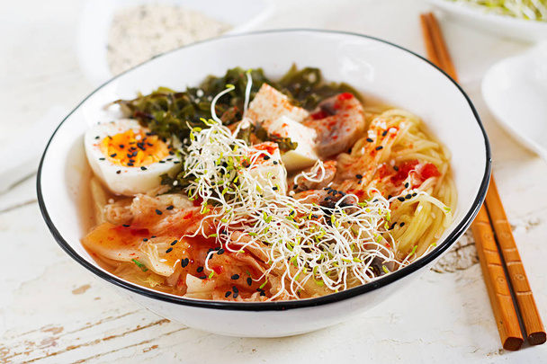 Miso Ramen Asian noodles with cabbage kimchi, seaweed, egg, mushrooms and cheese tofu in bowl on white wooden table. Korean cuisine. - Photo, Image