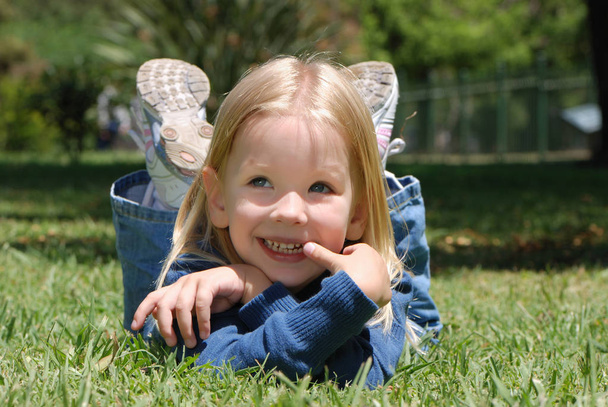 portrait of adorable little girl lying on grass in park - Photo, Image