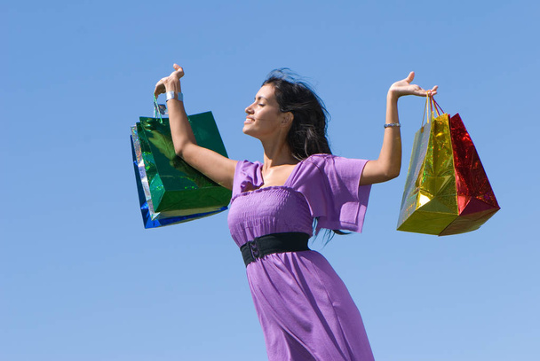 beautiful young woman holding colorful shopping bags in front of blue sky - Photo, image