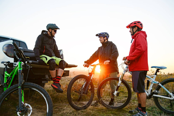 Friends Resting near Pickup Off Road Truck after Bike Riding in the Mountains at Sunset. Adventure and Travel Concept. - 写真・画像