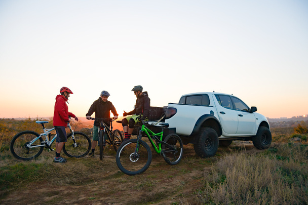 Friends Resting near Pickup Off Road Truck after Bike Riding in the Mountains at Sunset. Adventure and Travel Concept. - Фото, изображение