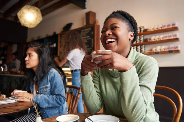 Młody African American kobieta śmieje się siedząc w kawiarni picia kawy i wychodzić z przyjaciółmi - Zdjęcie, obraz