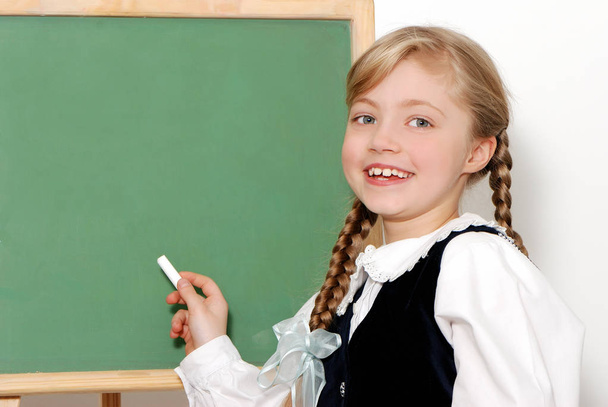 портрет красивой школьницы, рисующей на доске перед белой стеной
 - Фото, изображение