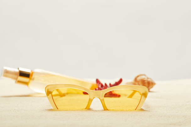 foyer sélectif de lunettes de soleil jaunes près de bouteille d'huile de bronzage sur sable doré isolé sur gris
 - Photo, image