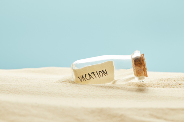 glass bottle with vacation lettering on paper in summertime isolated on blue - Photo, Image