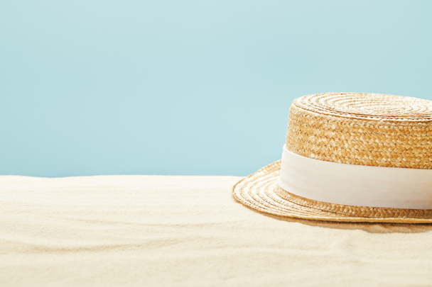 selective focus of straw hat on sandy beach in summertime isolated on blue - Photo, image