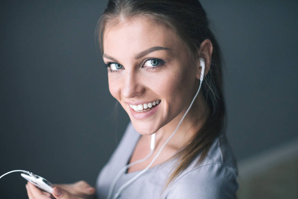 Happy young  smiling woman in earphones is listening to music with smart phone. - Фото, изображение