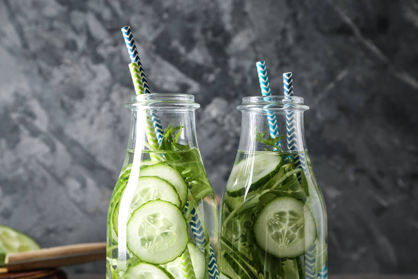 Flessen water van de komkommer op grijze achtergrond - Foto, afbeelding