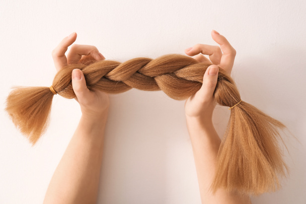 明るい背景に編み鎖と女性の手。髪の寄付の概念 - 写真・画像