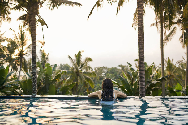 Woman in white swimsuit in outdoor pool on green jungle background - 写真・画像